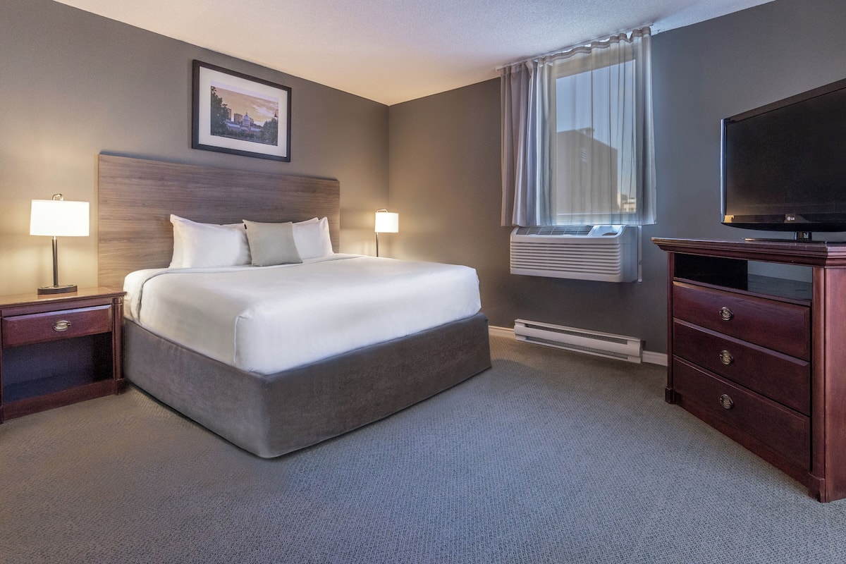 A hotel room with a large bed, two bedside lamps, a flat-screen TV, a dresser, and a framed picture on the wall.