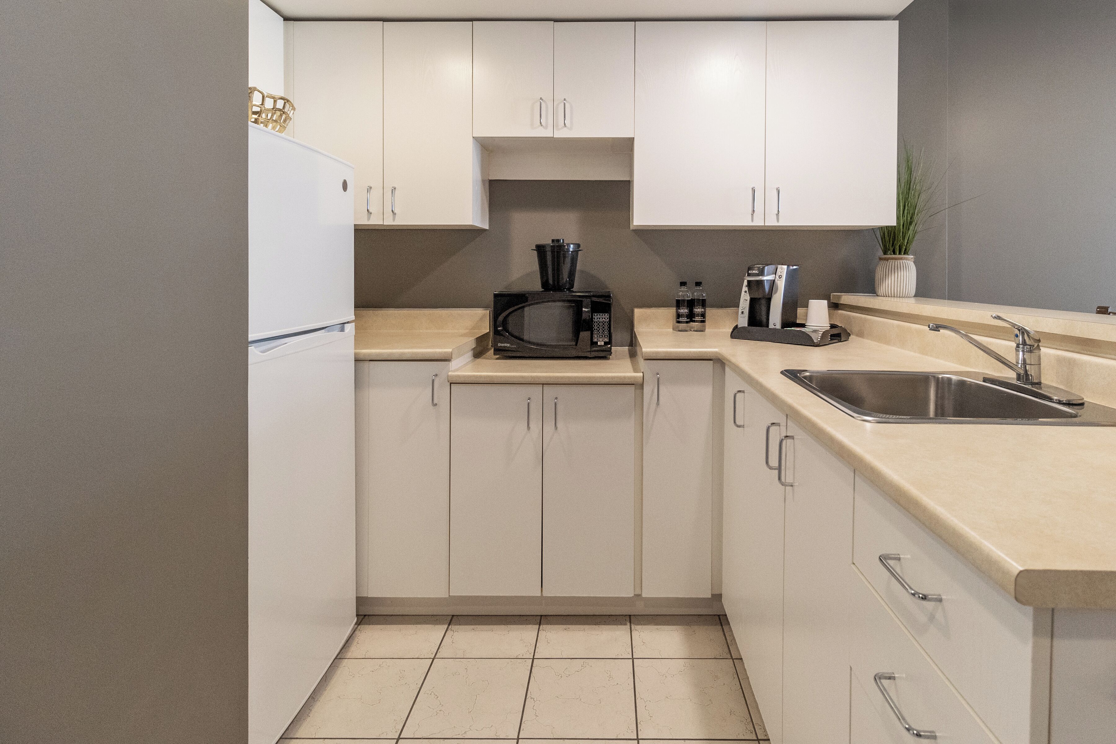 Una cocina moderna con armarios blancos, un lavamanos de acero inoxidable y un microondas.