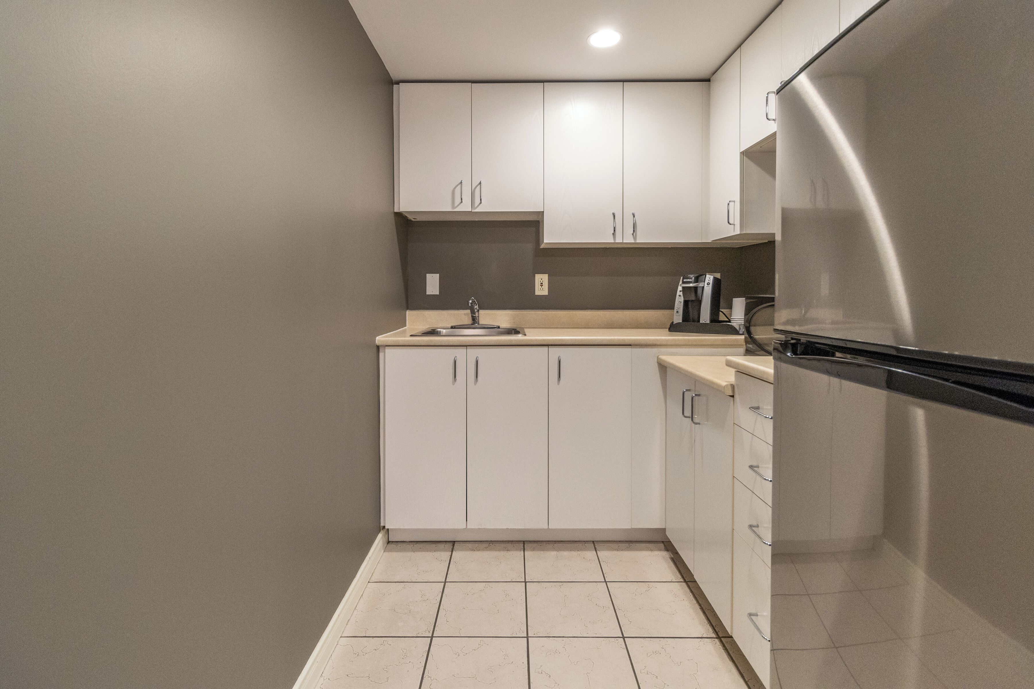 A modern kitchen with white cabinets, a stainless steel refrigerator, and a tiled floor.