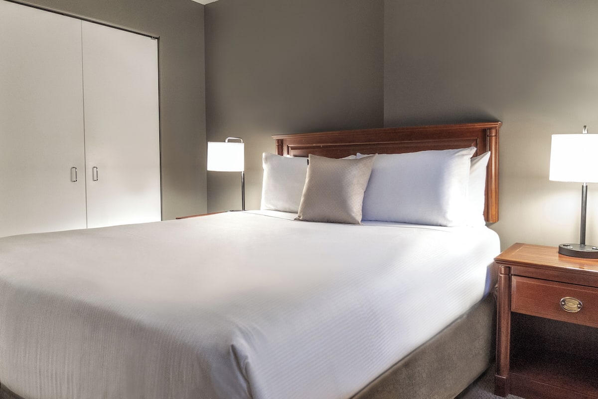 A neatly made bed with a wooden headboard, a bedside table with a lamp, and a wardrobe.