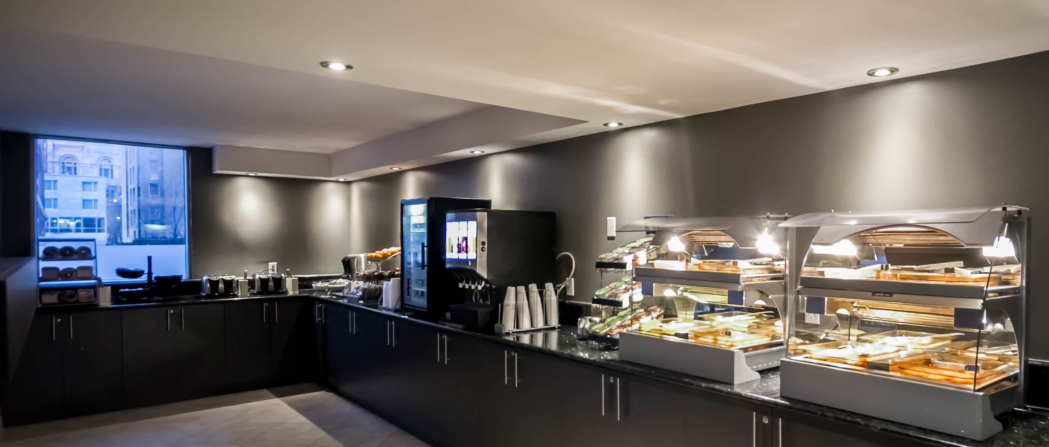 Une chambre d’hôtel moderne dotée d’une grande fenêtre, d’un minibar et d’un buffet proposant divers aliments pour le petit-déjeuner.