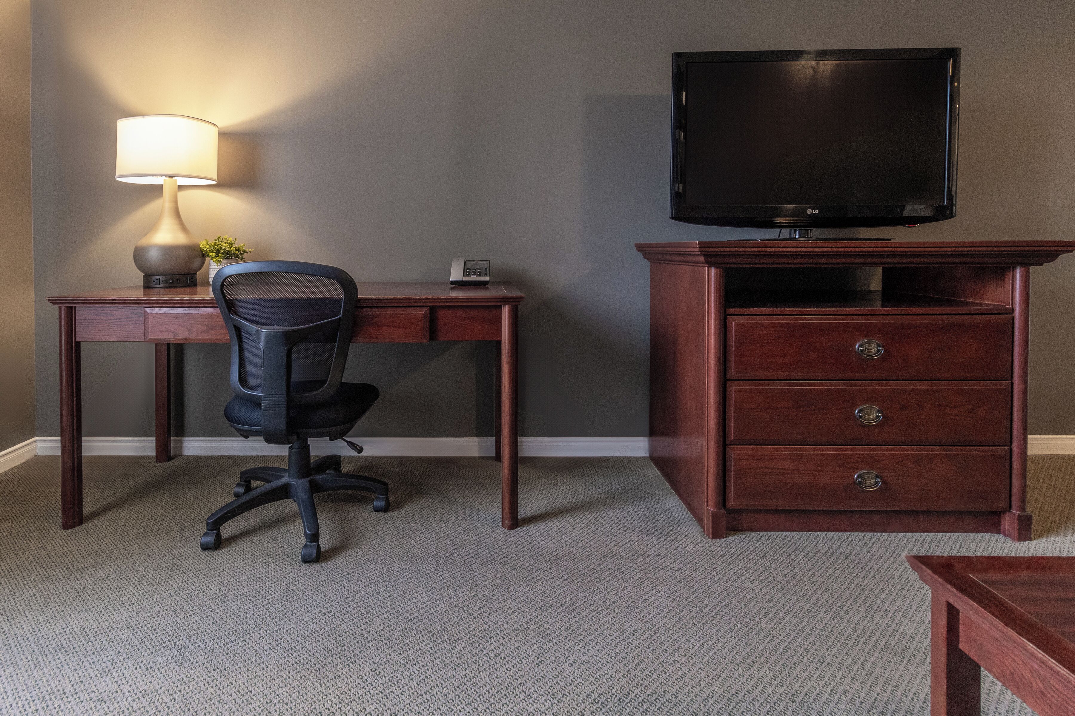 Una habitación con escritorio, silla, televisor y un mueble de madera.