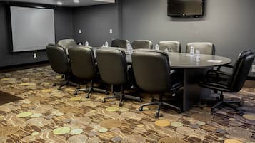 A conference room with a round table, six chairs, a projector screen, and a flat-screen TV on the wall.