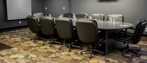 A conference room with a round table, six chairs, a projector screen, and a flat-screen TV on the wall.