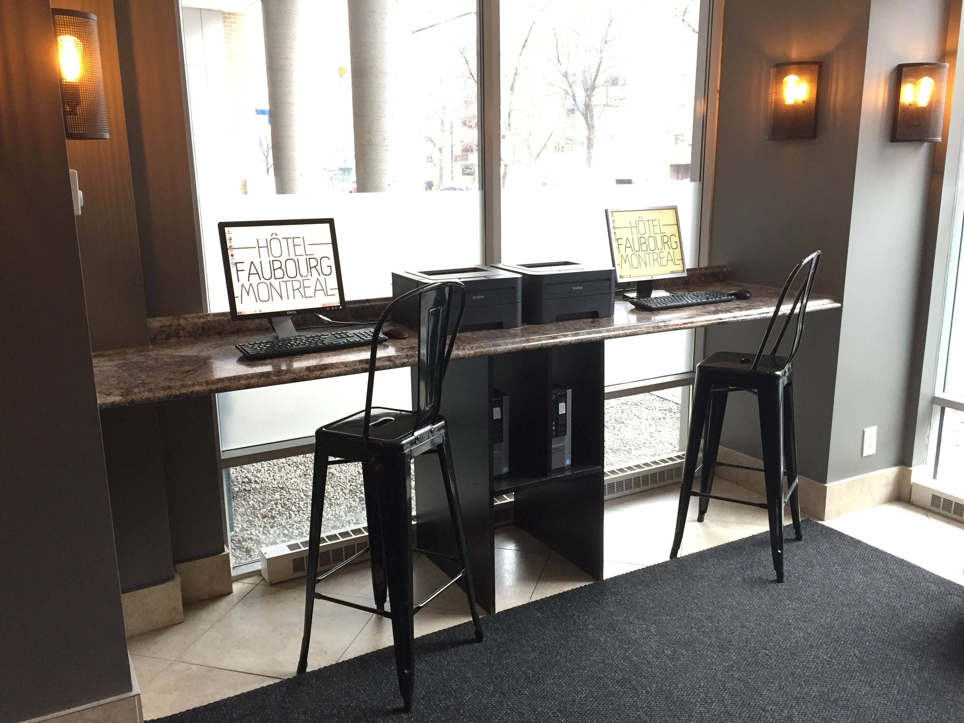A hotel reception desk with two computer stations, a black chair, and a sign indicating the hotel name.