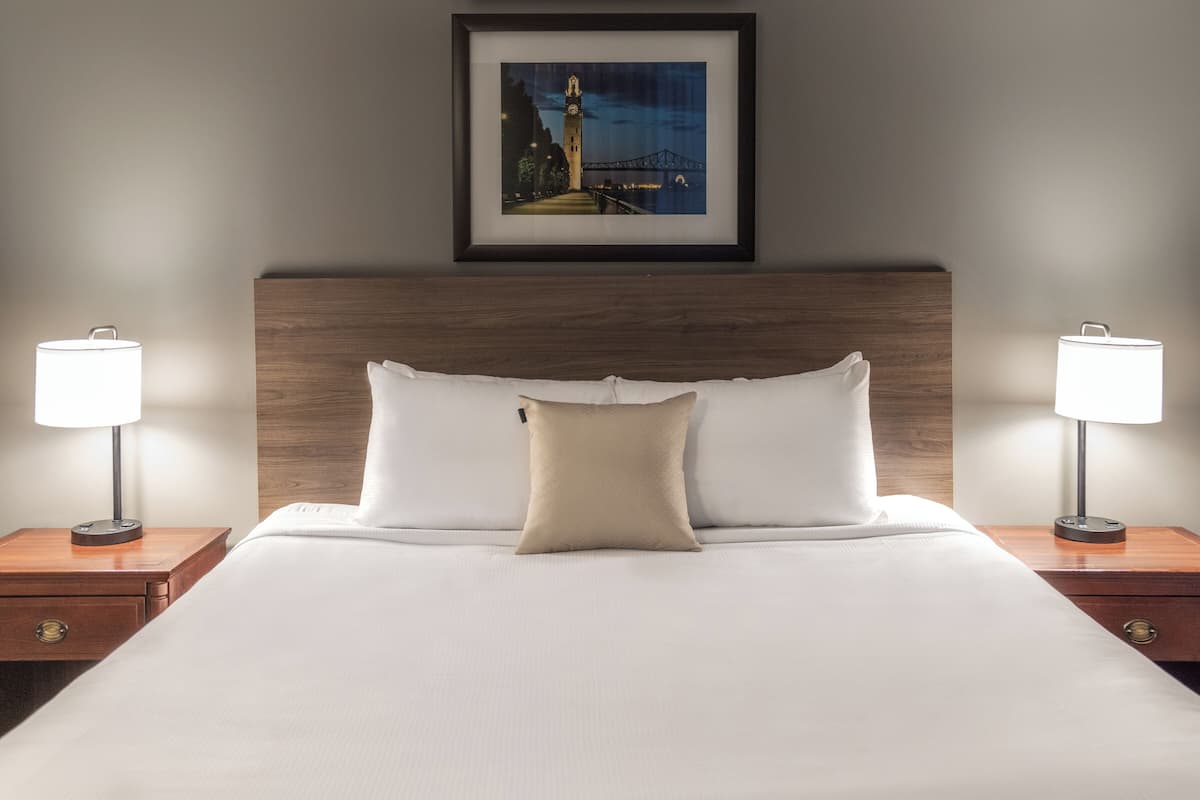A neatly made bed with white linens, a wooden headboard, and two bedside lamps.
