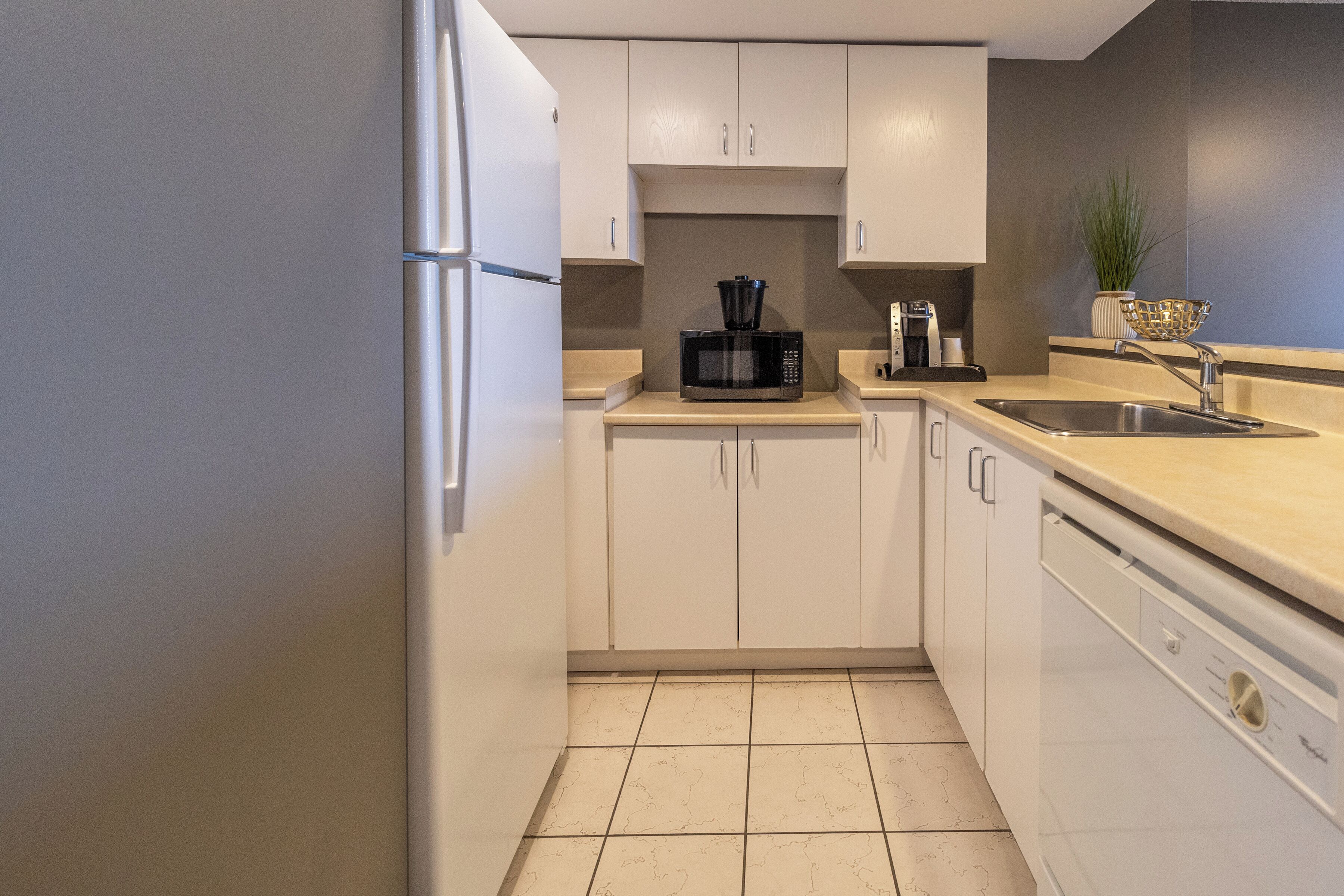 A modern kitchen with white cabinets, a black microwave, a coffee maker, and a dishwasher.