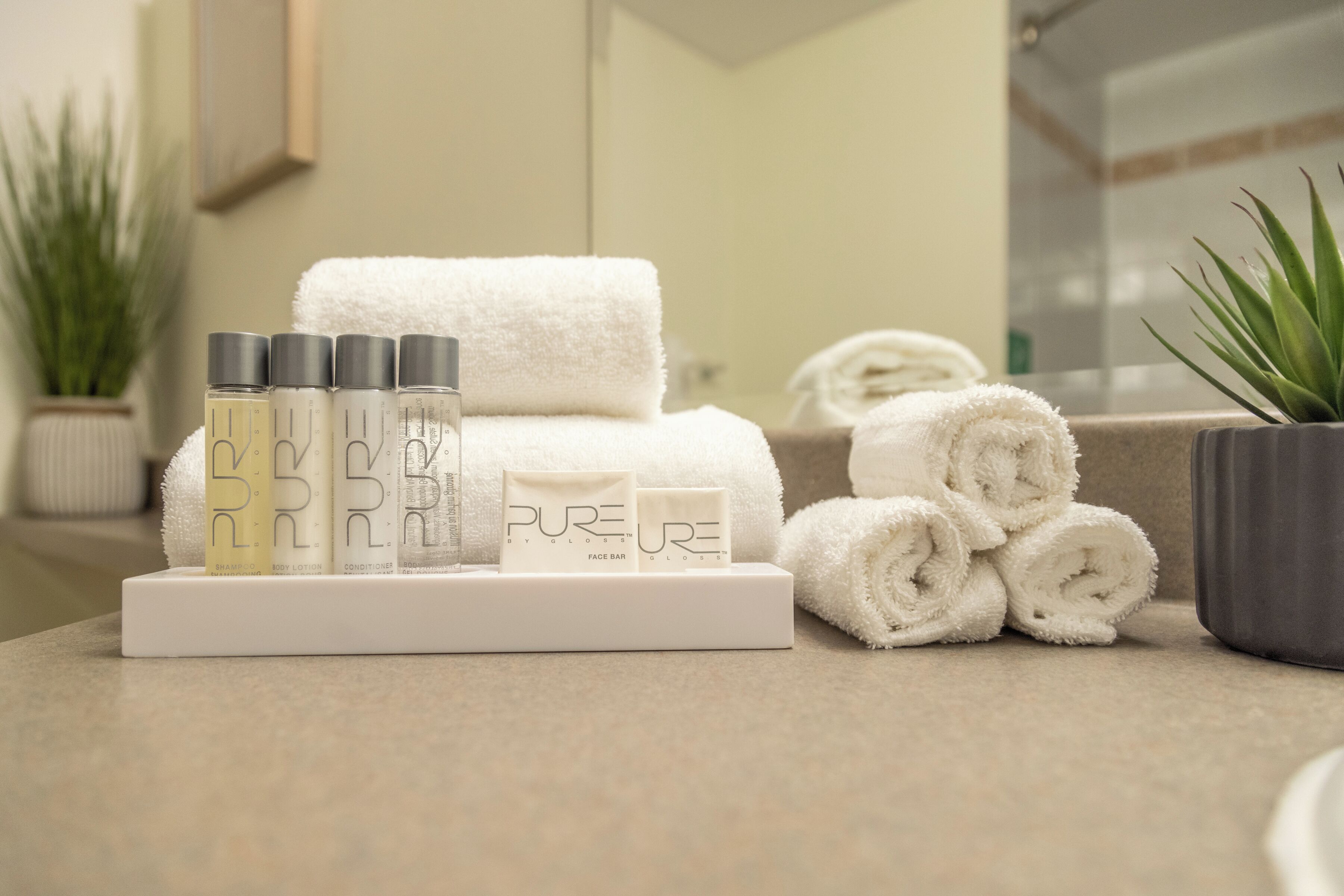Ein Badezimmer mit einem Stapel weißer Handtücher, aufgerollten Handtüchern und einer Schale mit Flaschen von Pure Körperlotion und Conditioner.