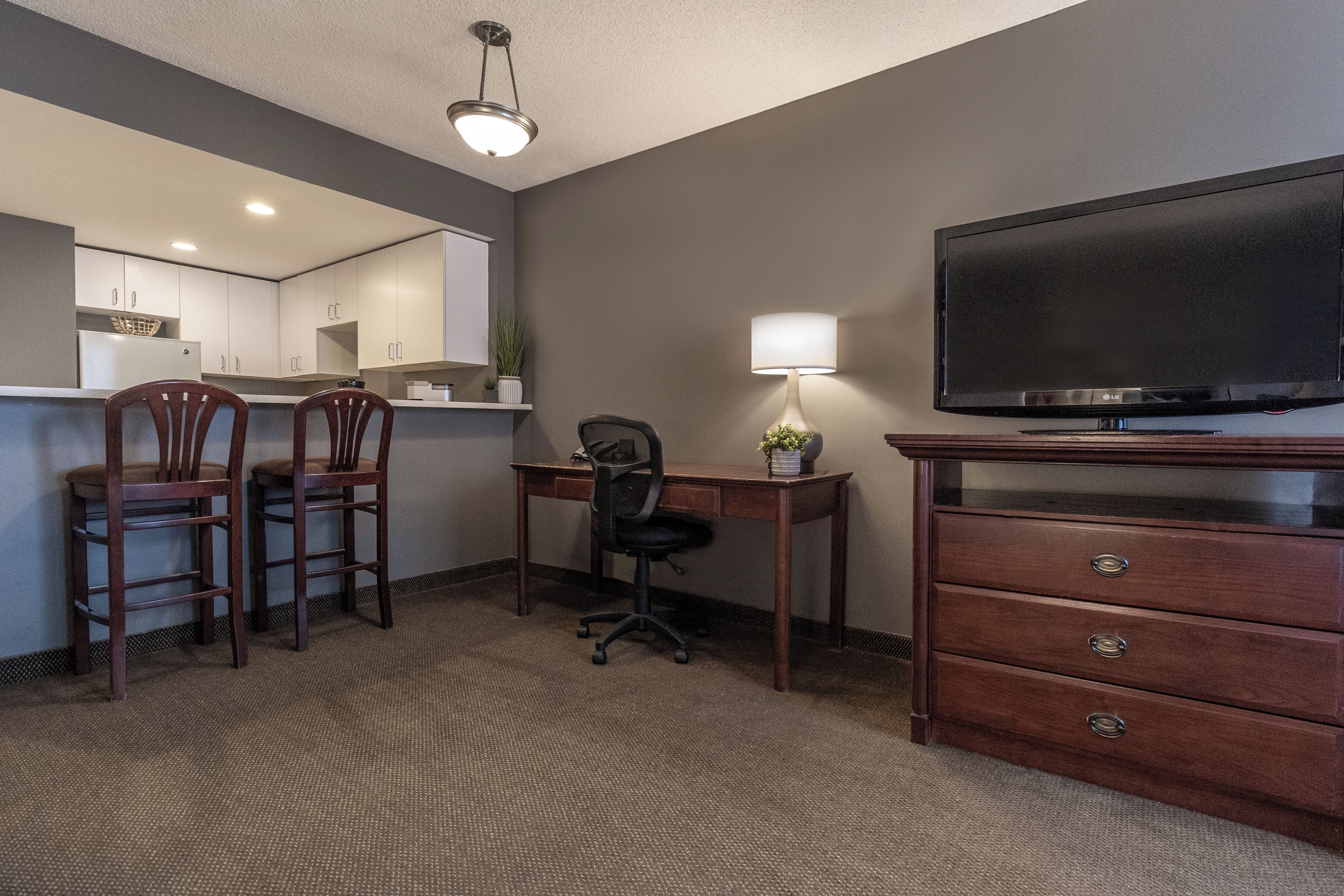 Una habitación de hotel con kitchenette, un escritorio con silla, televisor y cómoda.