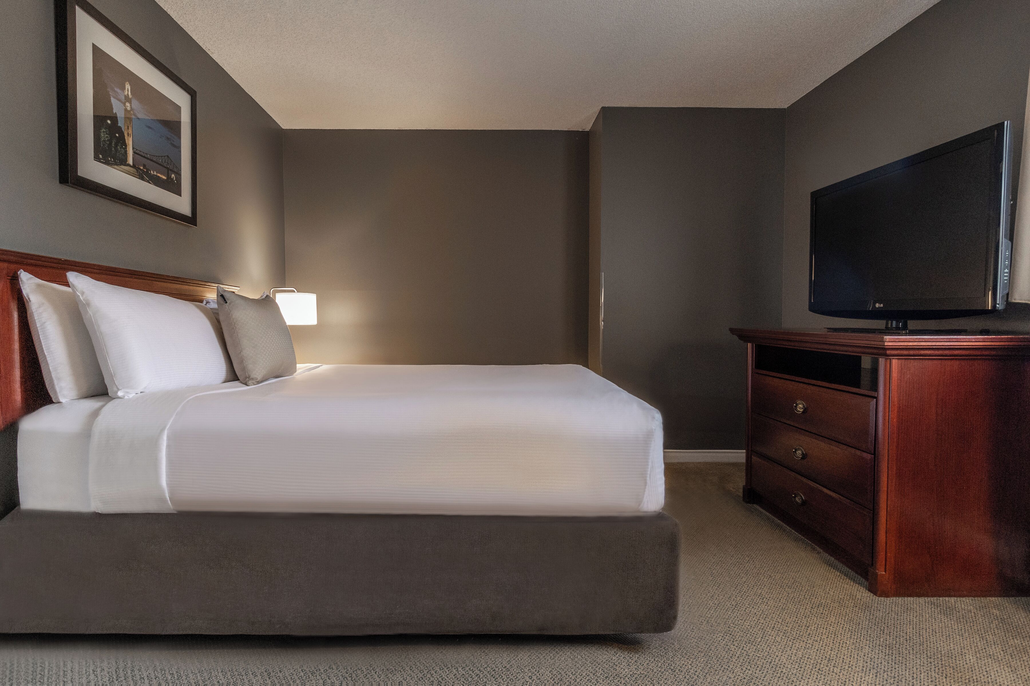 Habitación de hotel con cama, televisión, cómoda y un cuadro en la pared.