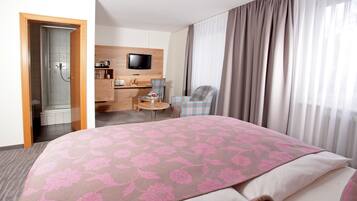 Quarto de hotel com uma cama grande, uma escrivaninha com cadeira, televisão e área de duche.