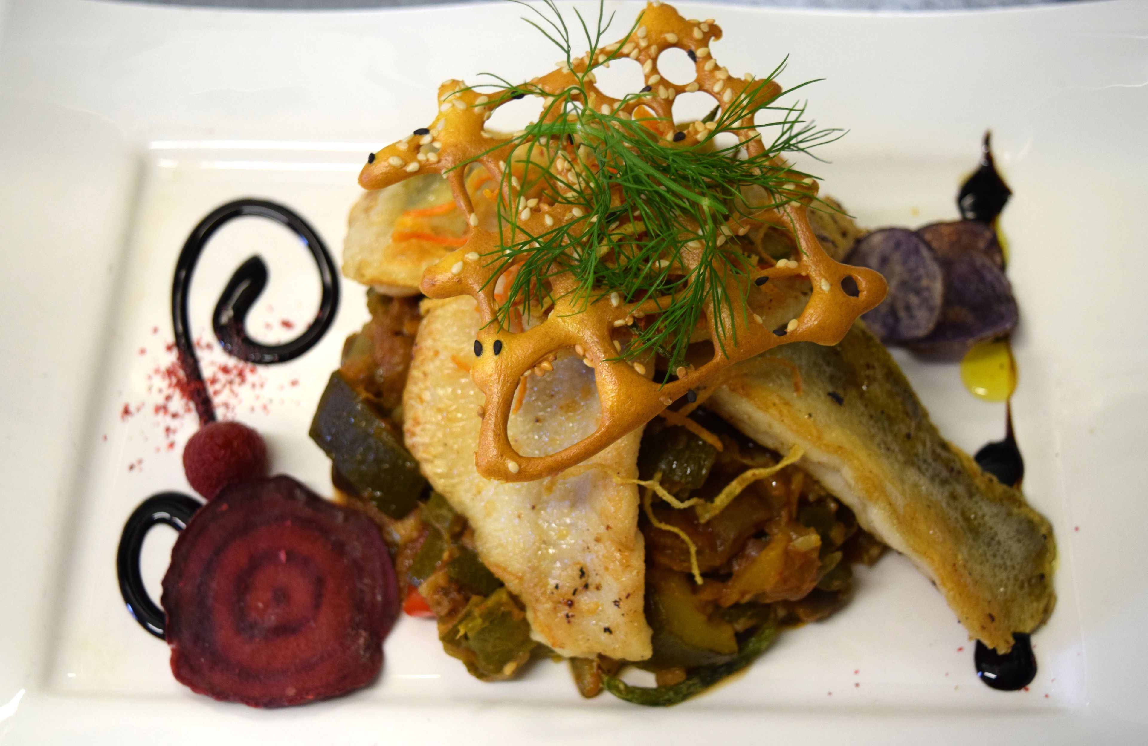 A dish with a fish fillet, vegetables, and decorative elements on a white plate.