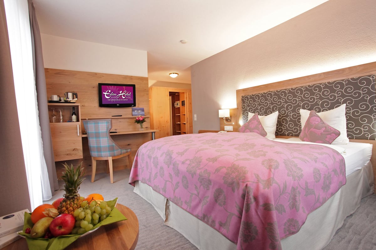Quarto de hotel com cama, escrivaninha com computador, televisão e cesta de frutas.