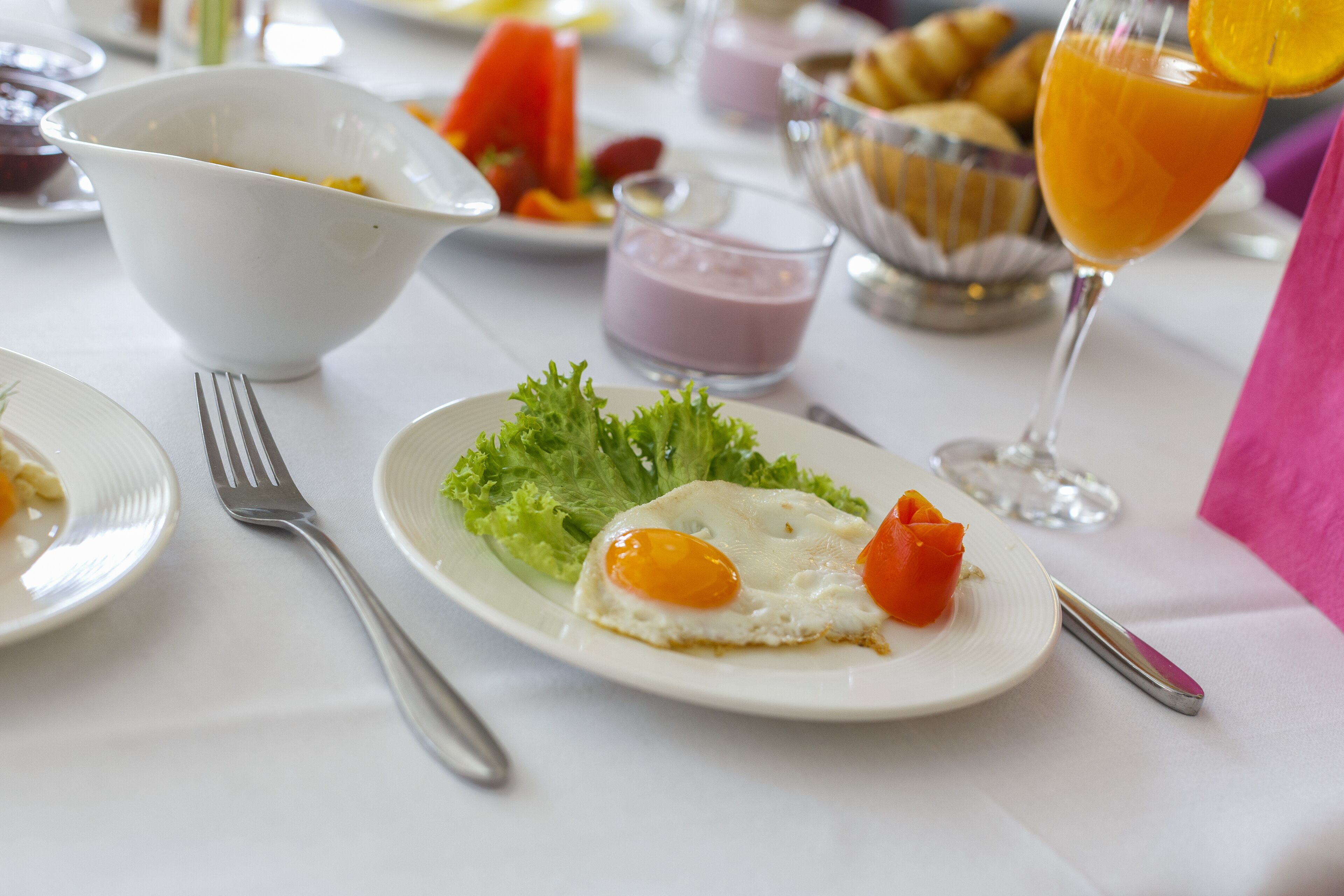 A breakfast setting with a plate of eggs, lettuce, and tomato, a bowl, and a glass of orange juice.