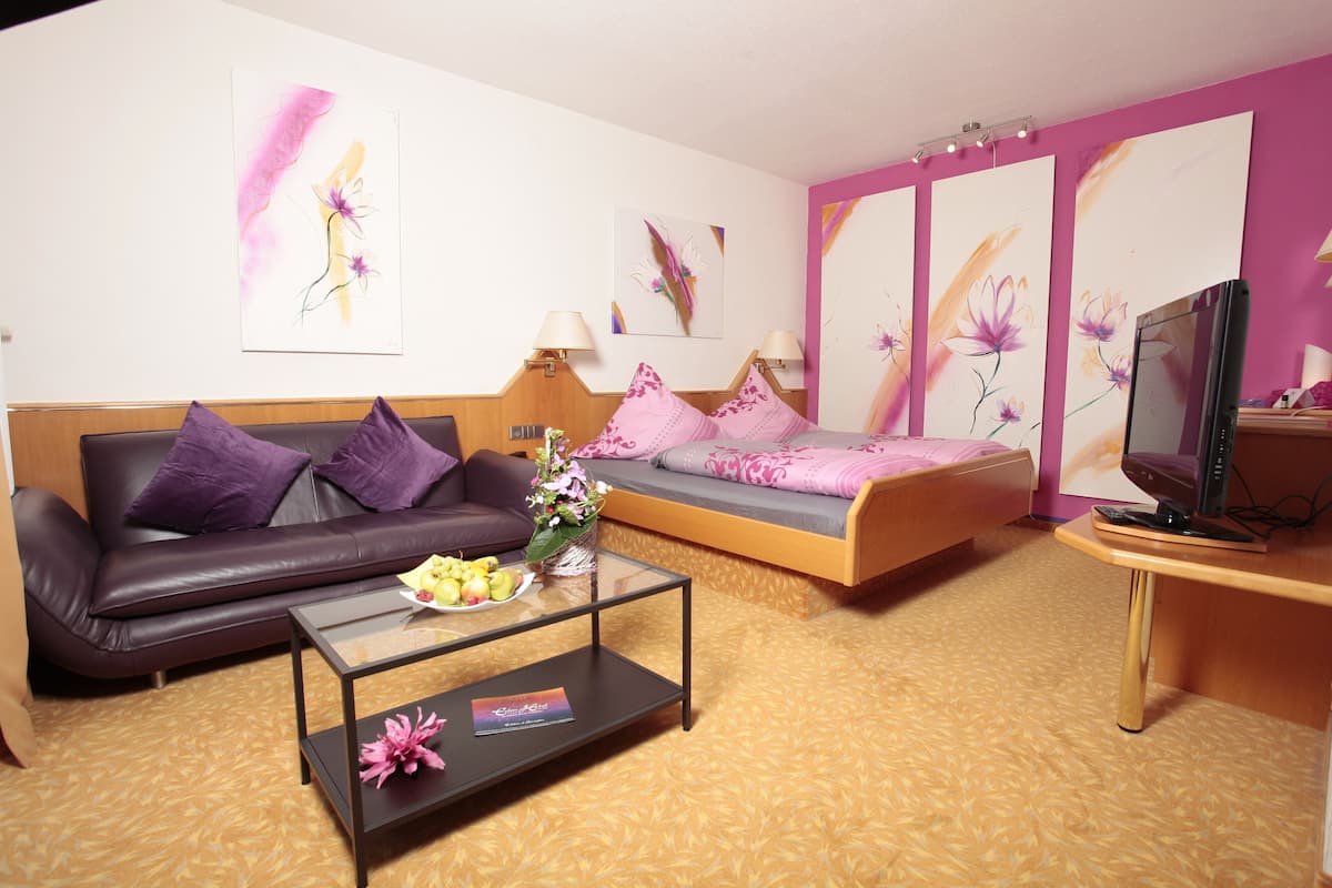 Quarto de hotel moderno com sofá, cama, pequena mesa com um vaso de flores e televisão em móvel.