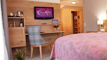 A hotel room with a bed, a desk with a chair, a TV, and a wooden wardrobe.