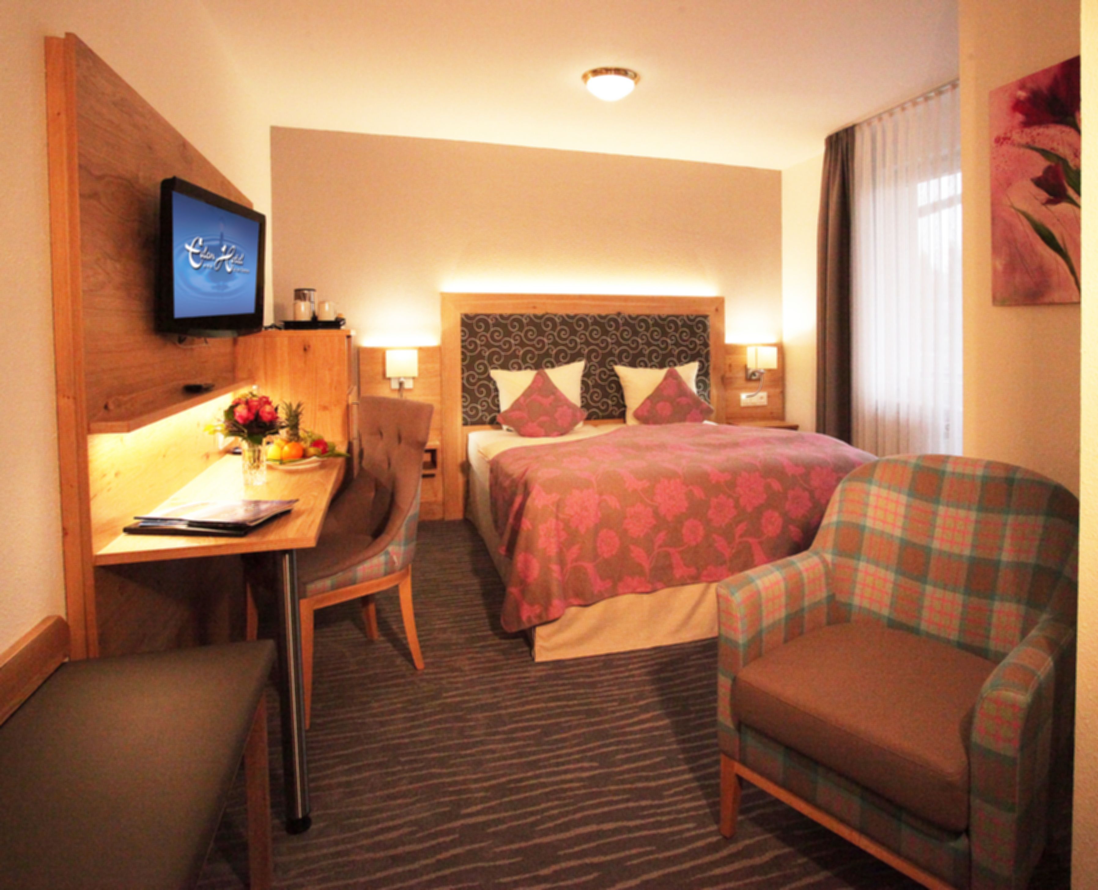 Habitación de hotel con cama, escritorio con computadora, silla y televisor en la pared.