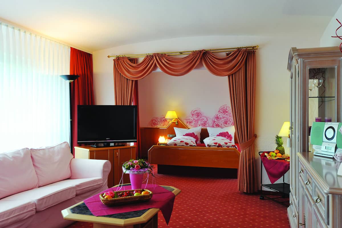Quarto de hotel com cama, televisão, sofá, mesa com fruta e abajur.