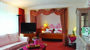 Una habitación de hotel con cama, televisión, sofá, una mesa con fruta y una lámpara.