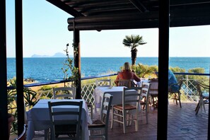 Un área de comedor al aire libre con mesas y sillas, con vista al mar.