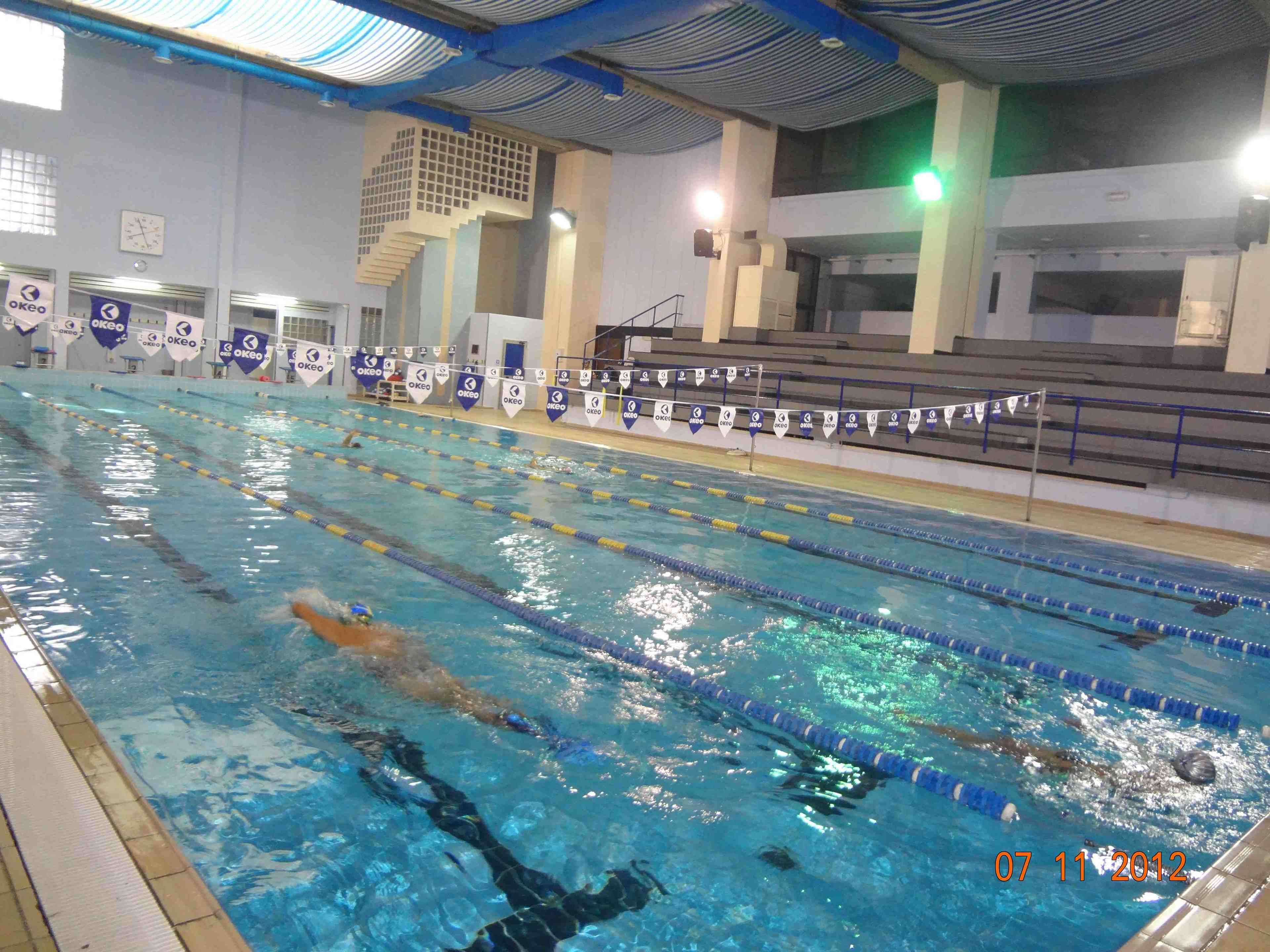 En indendørs swimmingpool med flere baner, et ur og bannere på væggene.