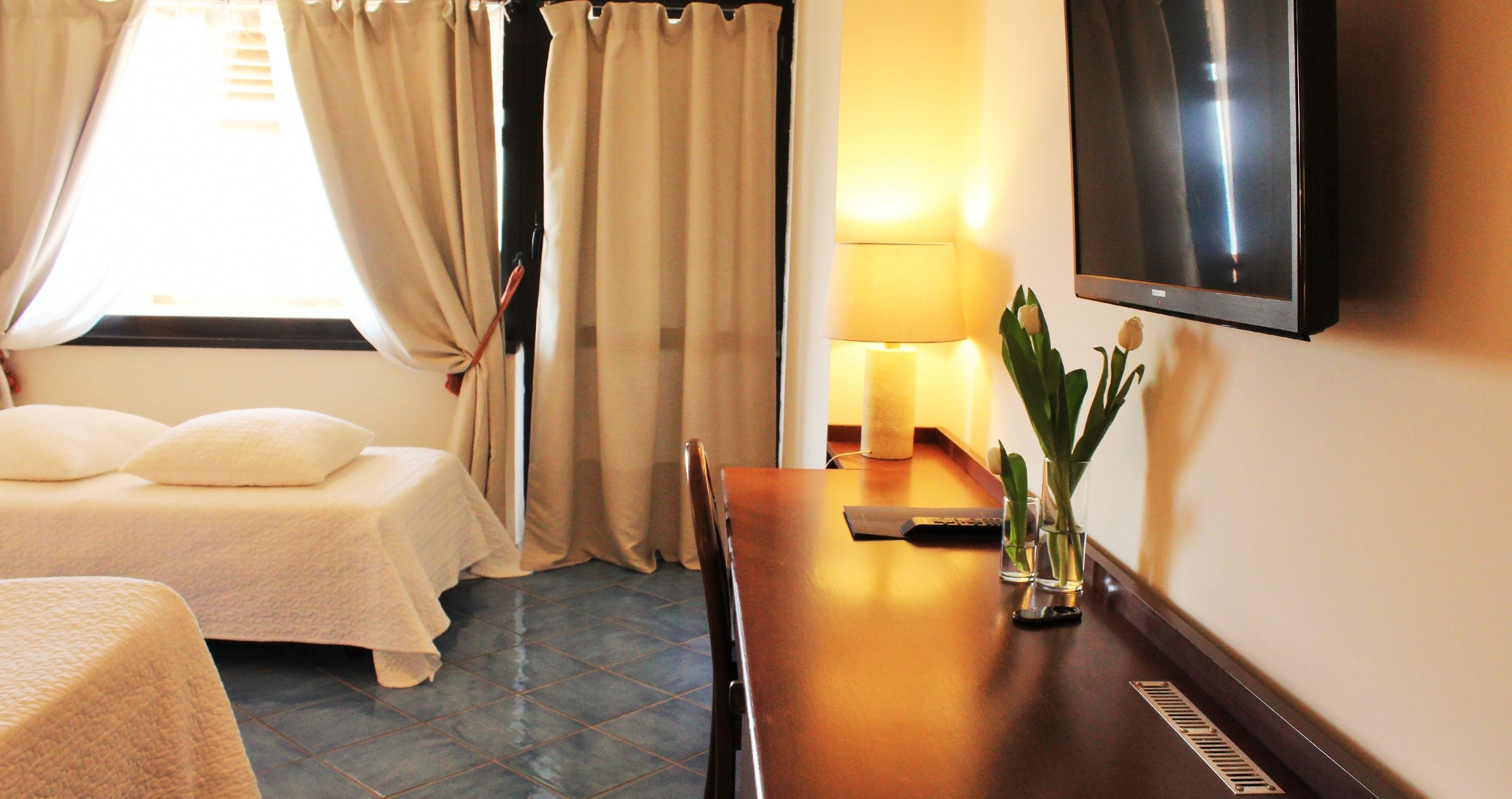 A hotel room with a bed, a desk with a lamp, a TV, and a window with curtains.