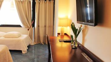 A hotel room with a bed, a desk with a lamp, a TV, and a window with curtains.