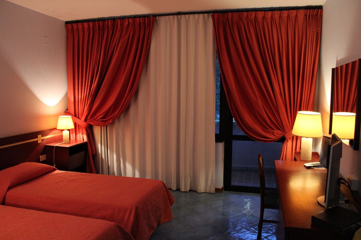 Habitación de hotel con dos camas, un escritorio, una silla, un televisor y cortinas.