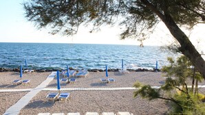 A beach with rows of sun loungers and umbrellas, a pebble beach, and a view of the sea. - Hotel Puntaquattroventi (Ercolano)