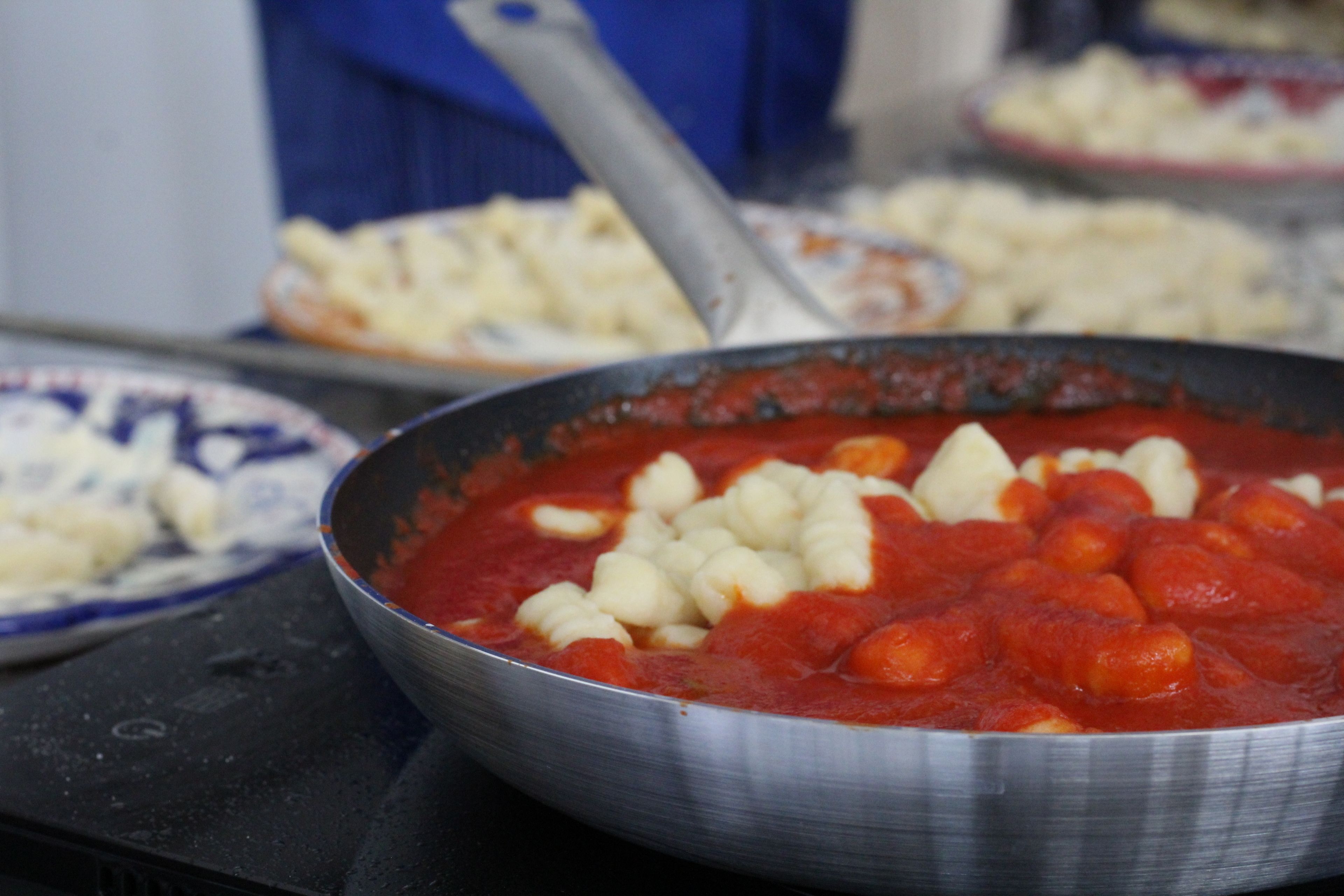 Un tazón de acero inoxidable lleno de salsa roja y alb óndigas blancas sobre una hornilla.