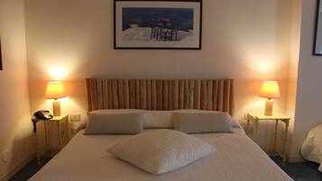 Una habitación de hotel con una cama grande, dos mesitas de noche con lámparas, un cuadro enmarcado en la pared y un cabecero de madera.