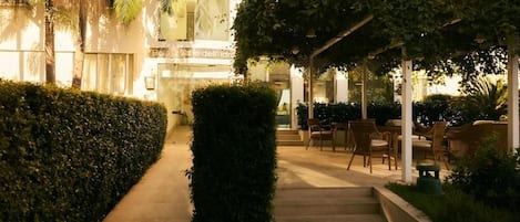 A well-lit outdoor area with a pathway leading to a covered seating area with chairs and tables.