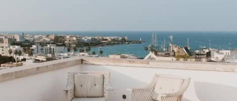 A rooftop terrace with wicker furniture and a view of the sea and cityscape.