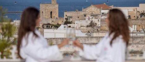 Two people in white lab coats overlooking a coastal town with historical buildings and a clear view of the sea.