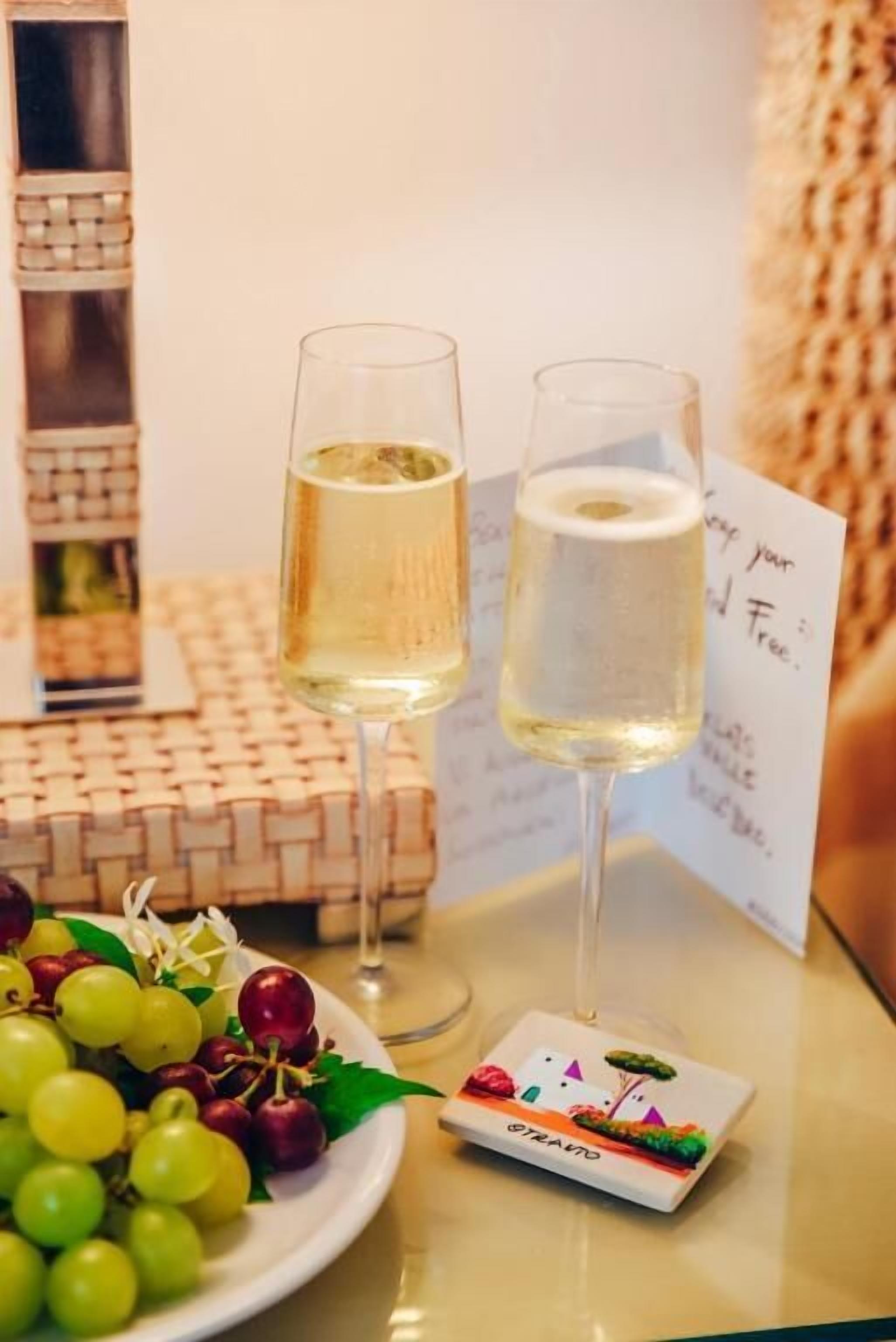 A table with two glasses of white wine, a plate of grapes and cherries, and a small card with a drawing.