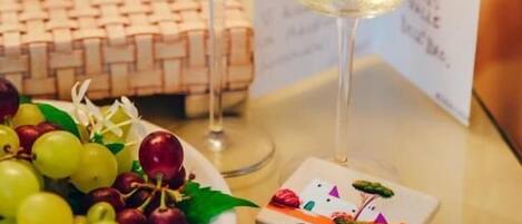 A table with two glasses of white wine, a plate of grapes and cherries, and a small card with a drawing.