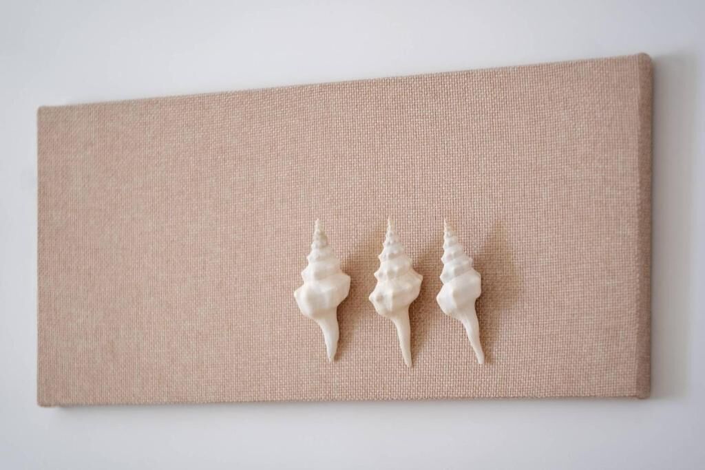 Pared beige con textura y tres adornos blancos con forma de concha.