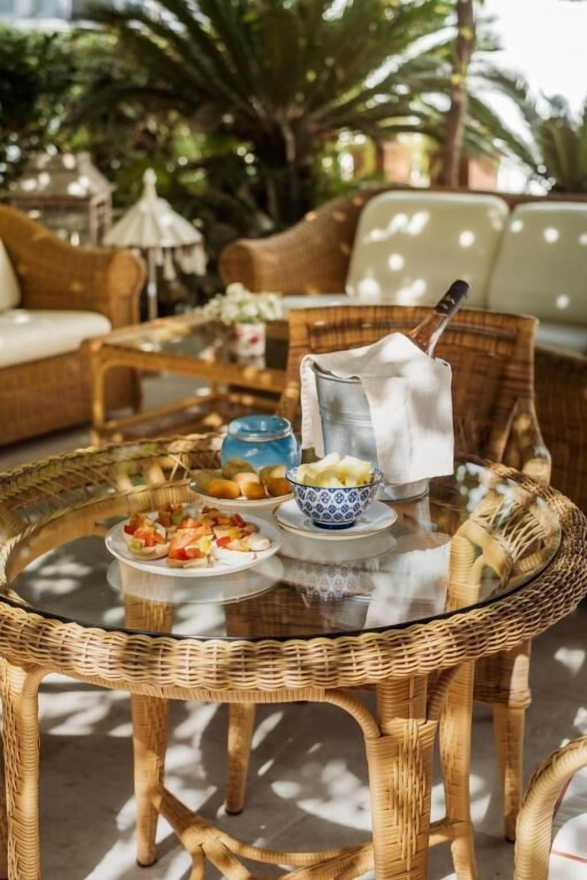 A wicker table with a glass top, surrounded by wicker furniture, and a bowl of fruit.