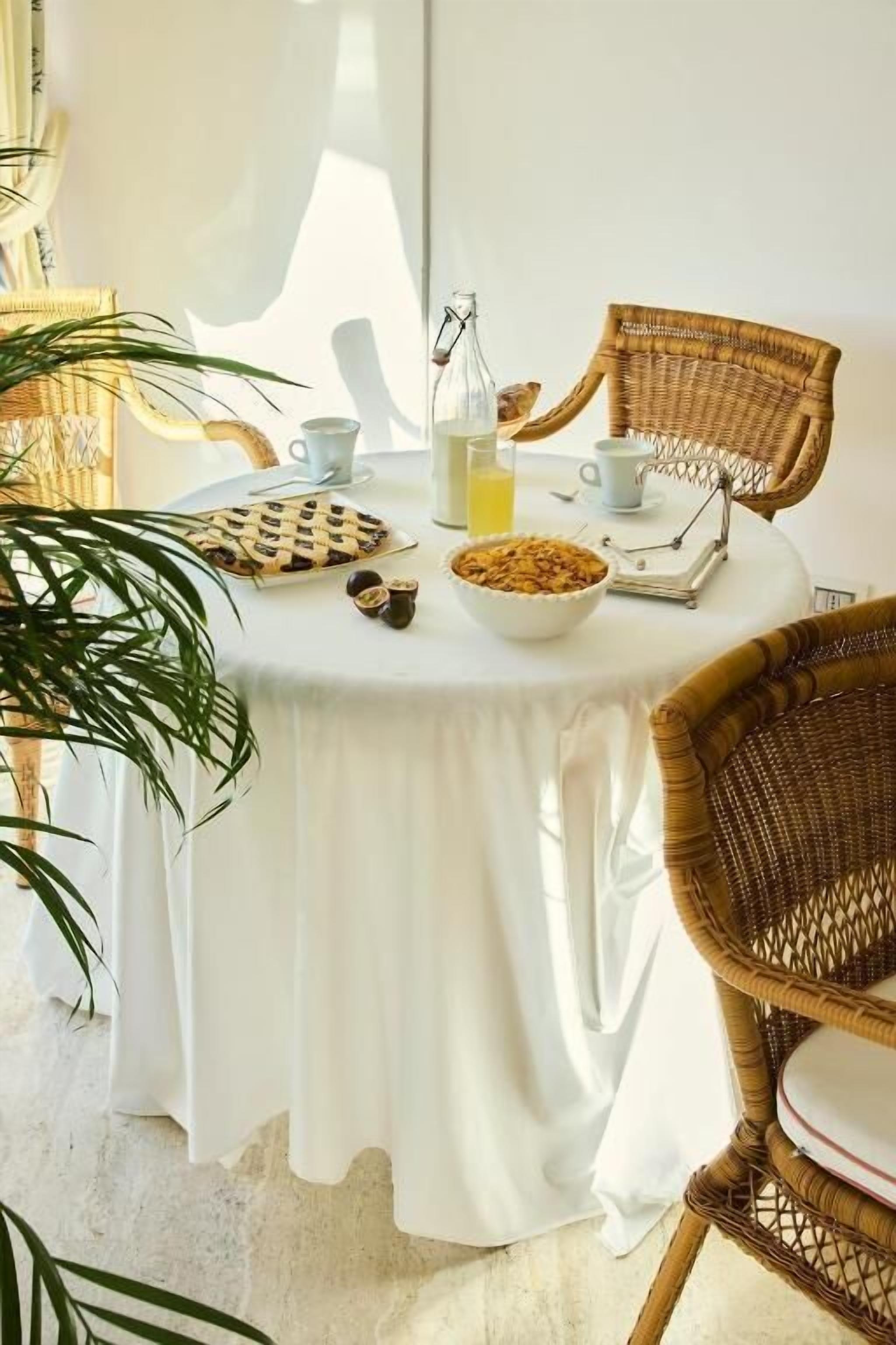 A round table with a white tablecloth, a bowl of cereal, a bottle of juice, and a cup.
