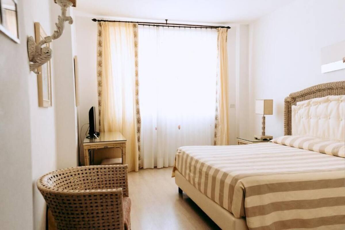 A hotel room with a bed, a television, a lamp, and a wicker chair.