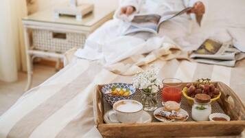 Bandeja de desayuno con café, pasteles y fruta sobre una cama, con un libro y una lámpara al fondo.