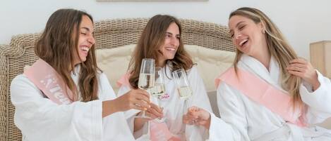 Three individuals seated on a bed with a woven headboard, holding glasses of champagne.