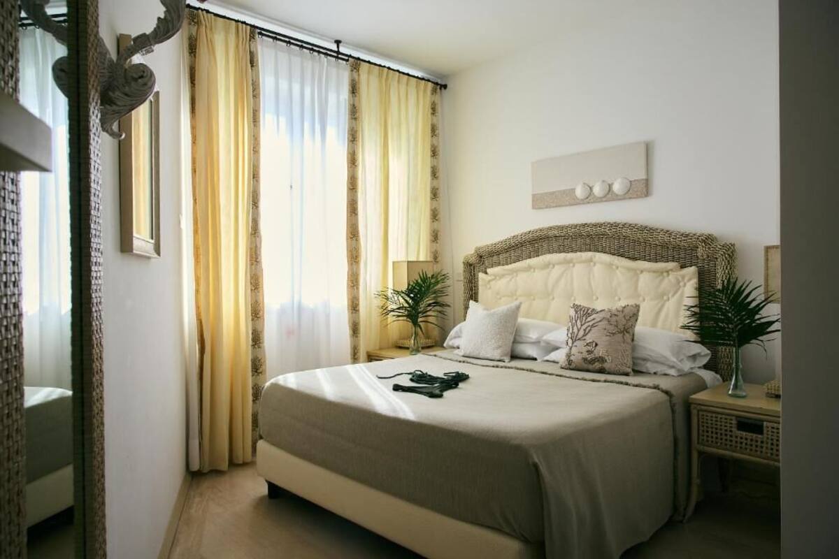 A bedroom with a large bed, two bedside tables, a mirror, and curtains.