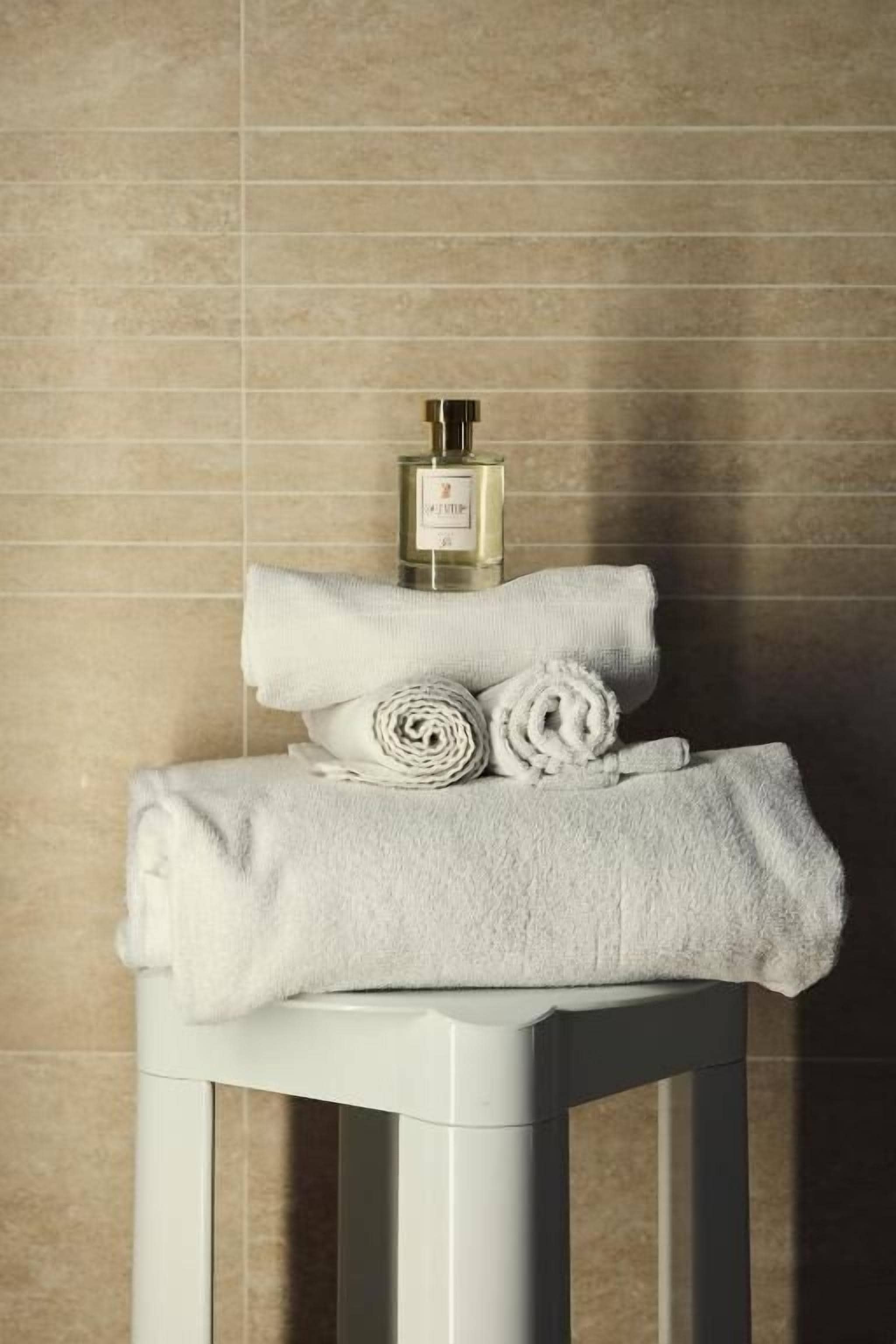 Un baño con un toallero blanco que sostiene toallas enrolladas y una botella de perfume.