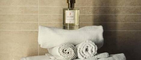 Un baño con un toallero blanco que sostiene toallas enrolladas y una botella de perfume.