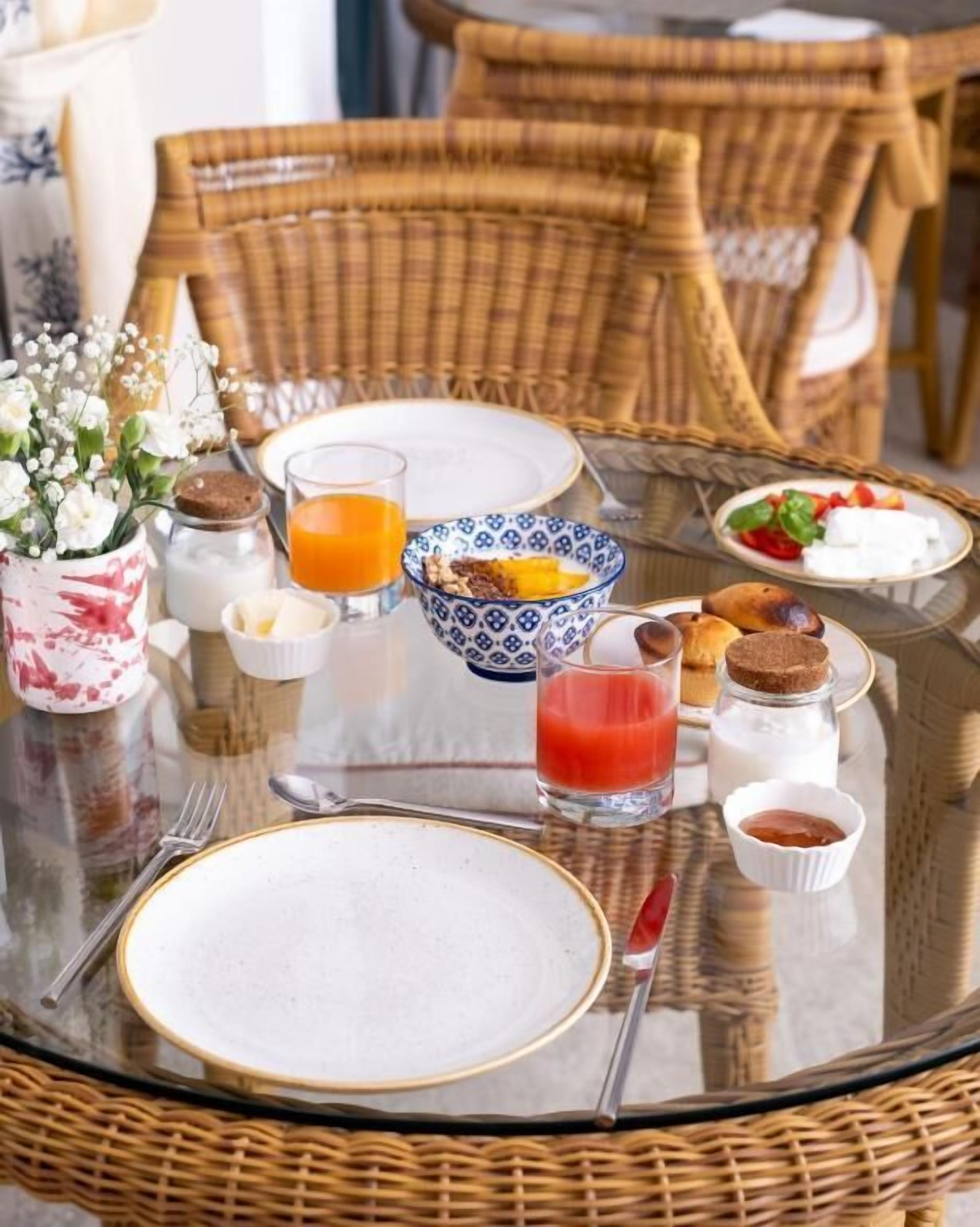 Une table de petit-déjeuner avec des chaises en osier, une table en verre et divers aliments pour le petit-déjeuner, notamment des toasts, des œufs et du jus de fruits.