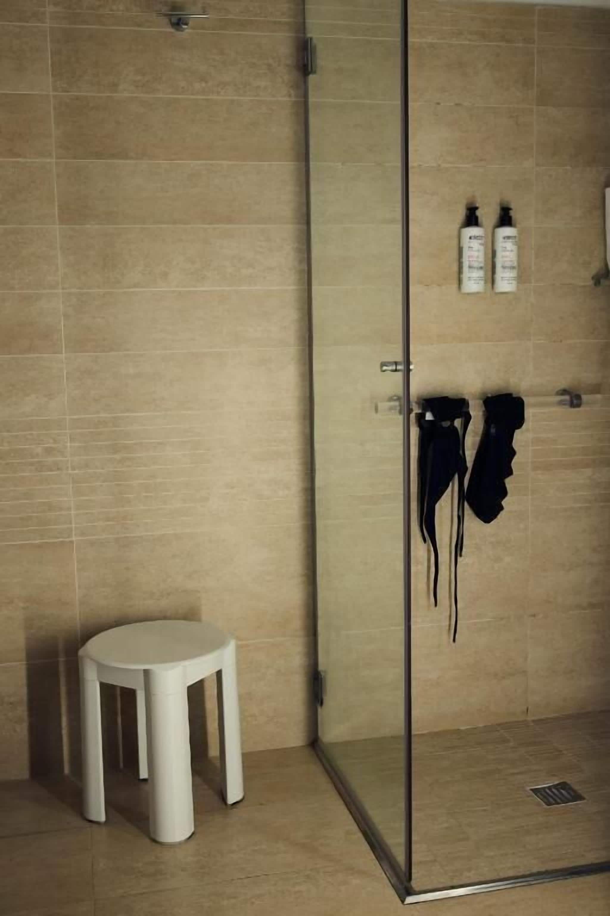 Une salle de bain avec une douche à parois de verre, un tabouret blanc et des articles de toilette fixés au mur.