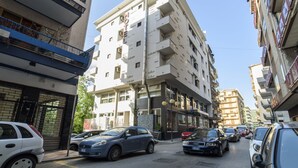 A multi-story building with balconies, a visible entrance, and parked cars along the street. - Hotel Palace (Battipaglia)