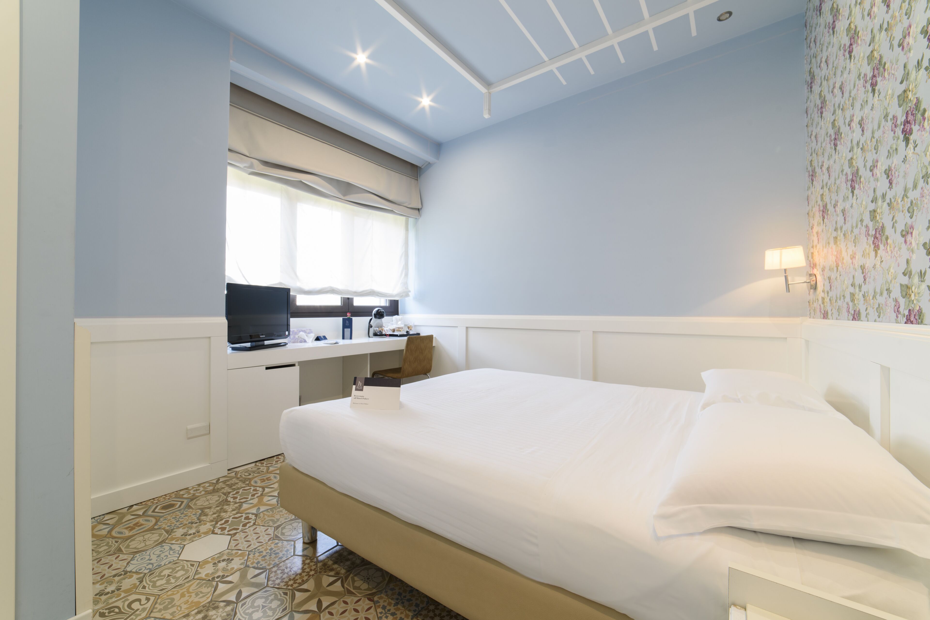 Un dormitorio con cama, un escritorio con computadora y una ventana con persianas.