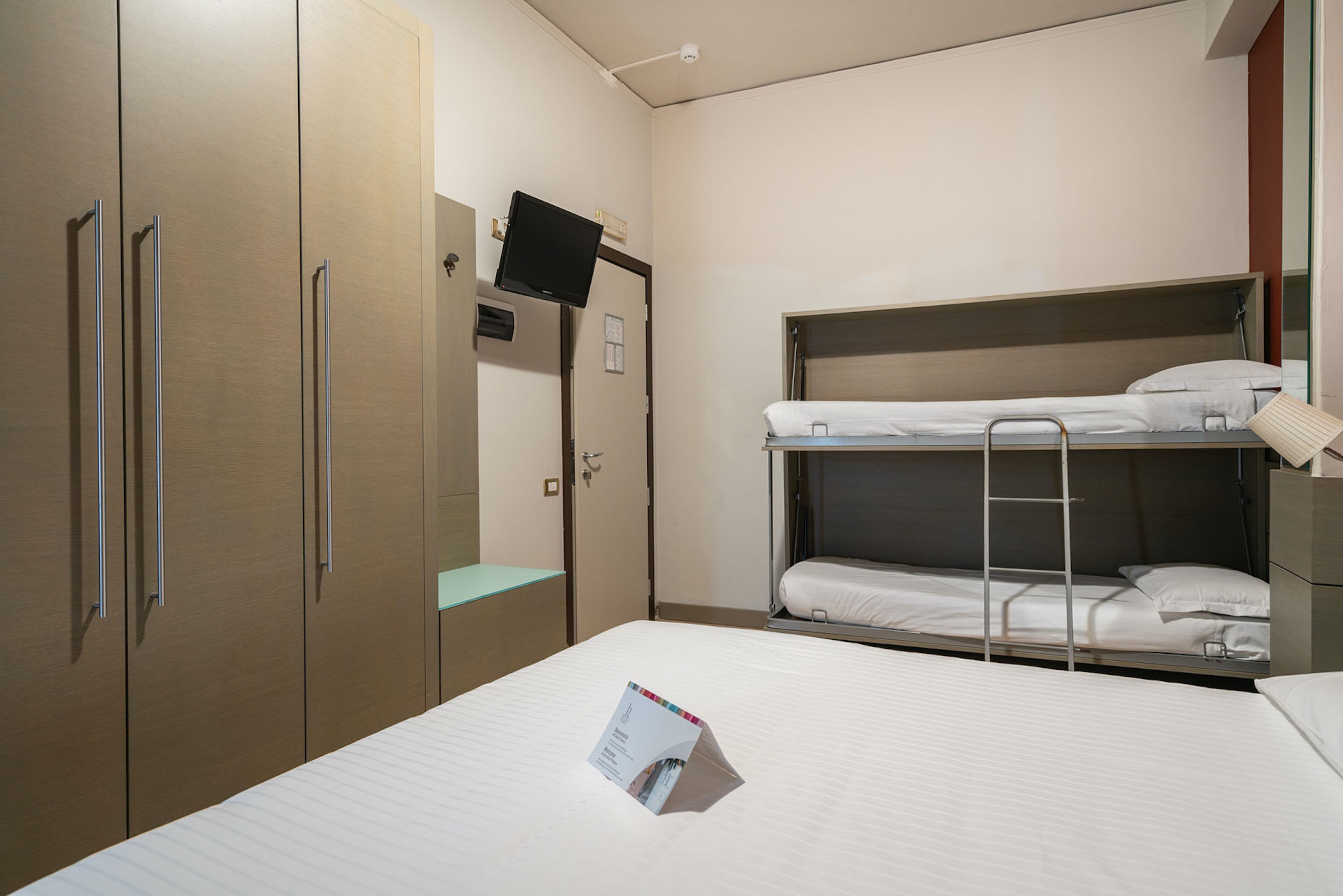 Una habitación de hotel con una cama litera, un escritorio con silla, un armario y un televisor de pantalla plana montado en la pared.